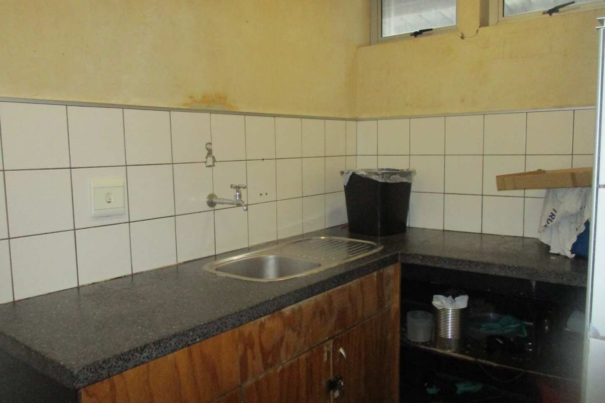A small kitchenette area featuring a stainless steel sink, tiled splashback, and wooden cabinetry in need of maintenance and cosmetic updates.