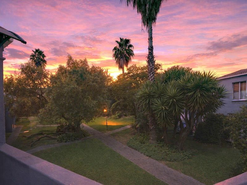 A scenic view of the apartment complex garden at sunset, featuring landscaped lawns, mature trees, and paved walkways.
