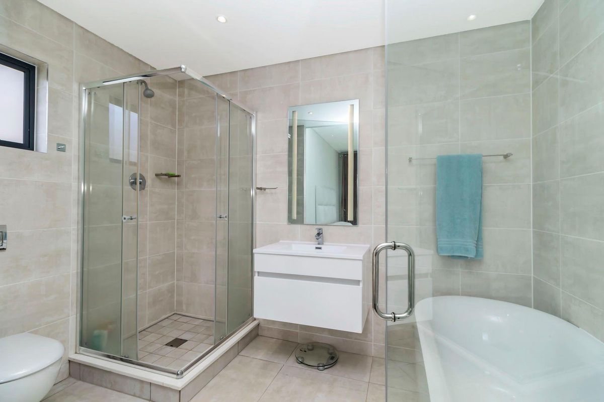 Modern bathroom featuring a glass-enclosed shower, a wall-mounted vanity with basin, and a separate bathtub with neutral floor-to-ceiling tiling.