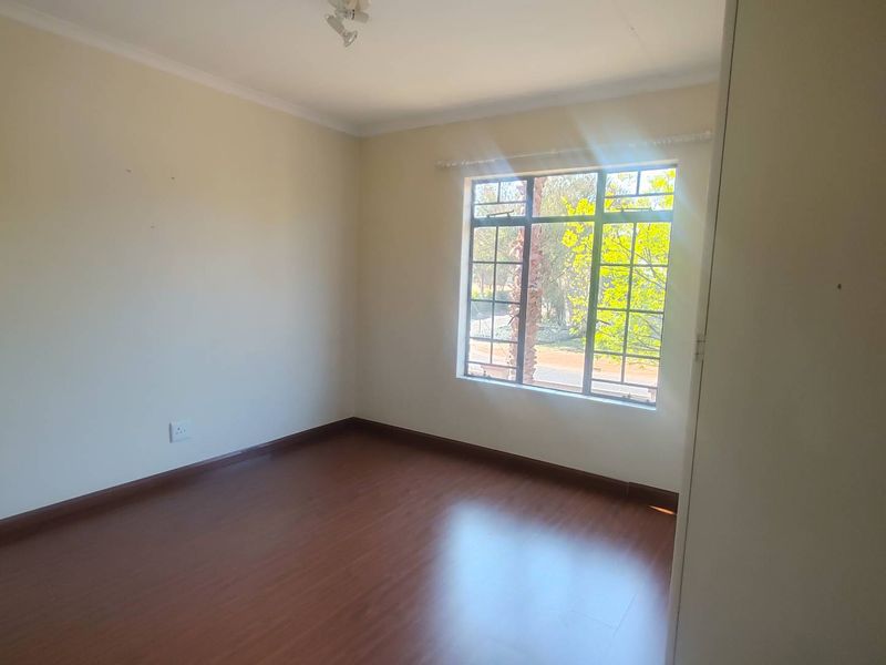 A bright, empty bedroom featuring laminate flooring, a built-in cupboard, and a window with security bars, offering a clean canvas for personalization.