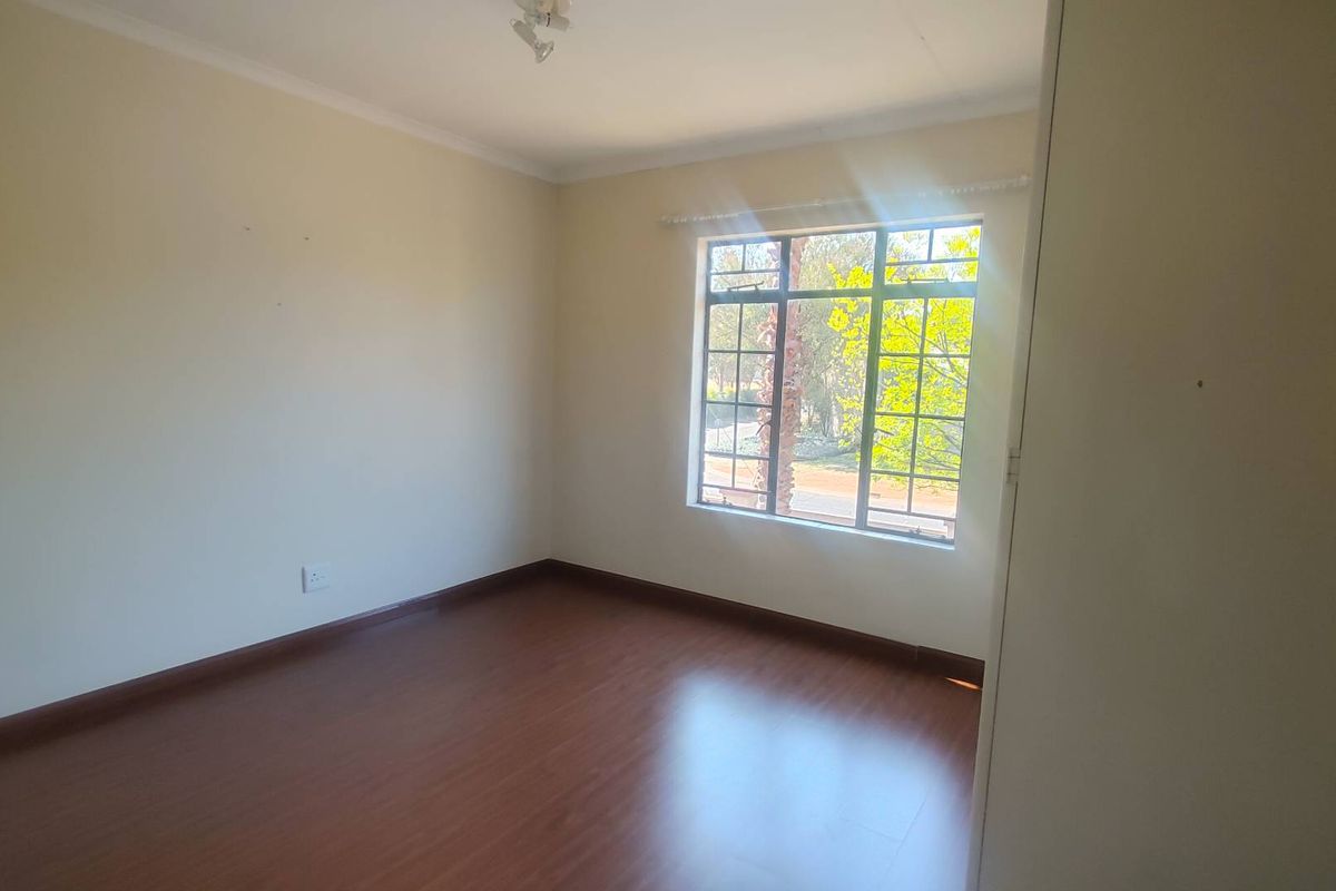 A bright, empty bedroom featuring laminate flooring, a built-in cupboard, and a window with security bars, offering a clean canvas for personalization.