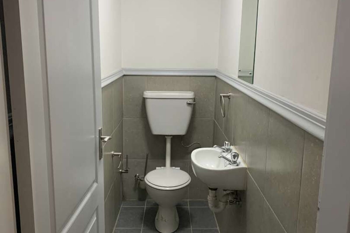 A compact industrial restroom featuring a wall-mounted basin, toilet, tiled lower walls, and a drop ceiling.
