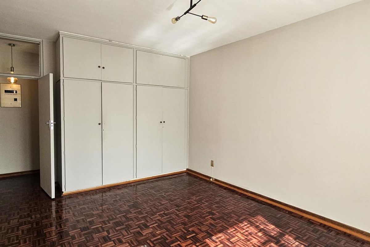 An empty bedroom featuring classic parquet flooring and ample built-in cupboard storage, providing a neutral canvas for personalization.