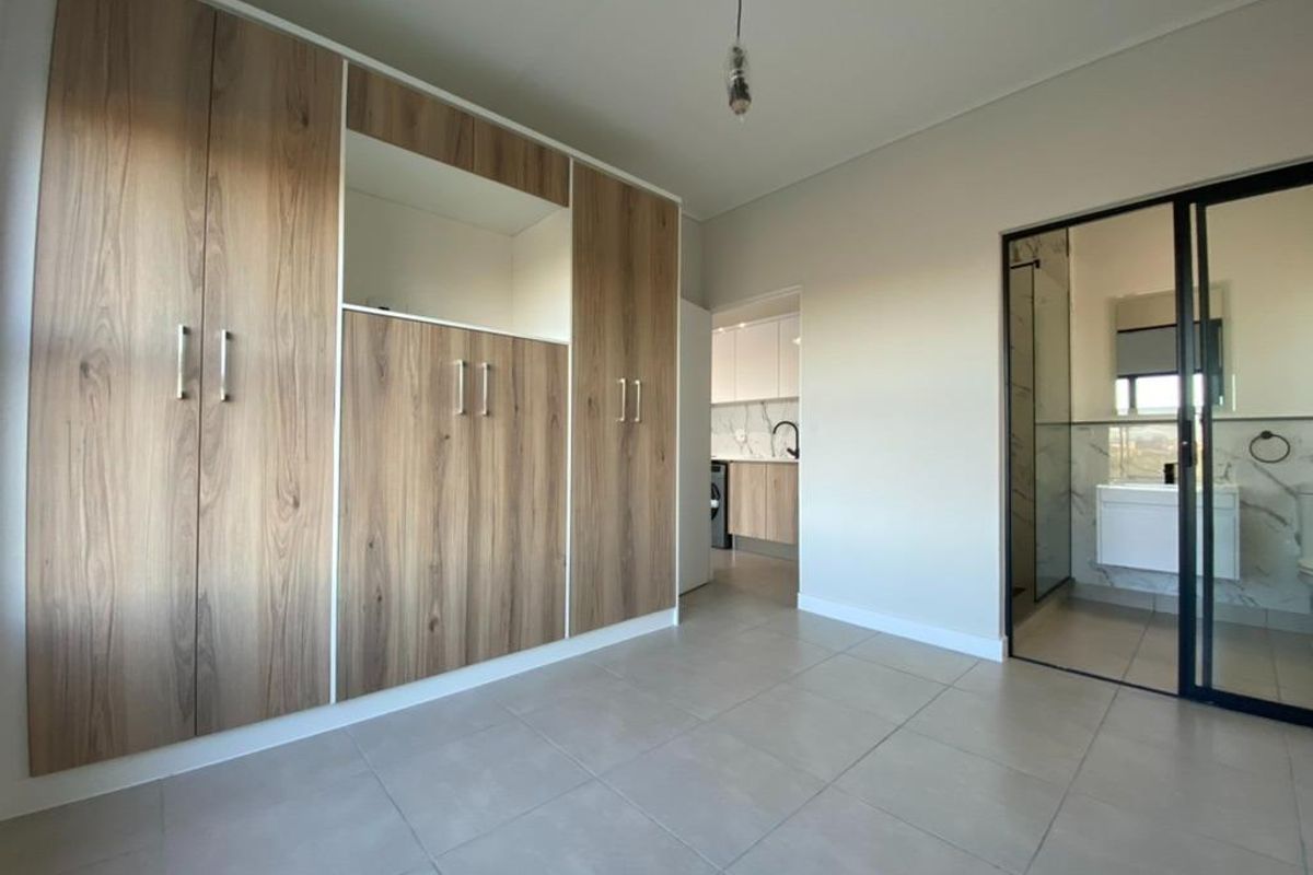 A modern bedroom featuring built-in wood-finish cabinetry and an en-suite bathroom with a glass-enclosed shower, showcasing clean lines and contemporary finishes.