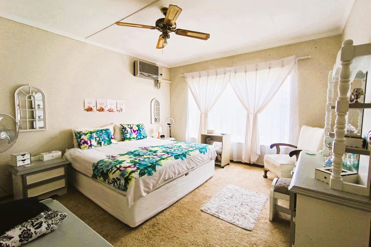 A spacious bedroom featuring a ceiling fan, wall-mounted air conditioning unit, and large windows with natural light.
