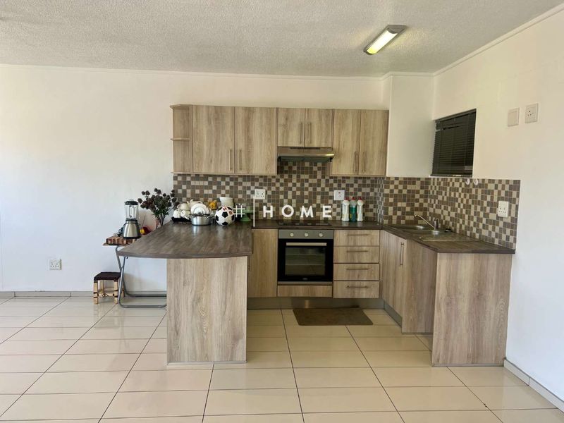 A functional kitchen featuring light wood-look cabinetry, a built-in oven with extractor fan, mosaic tile backsplash, and neutral ceramic floor tiles.