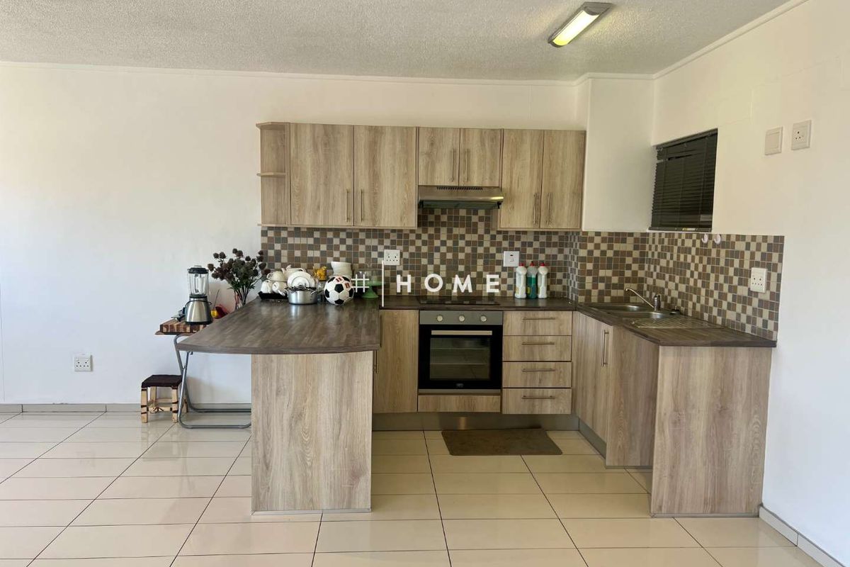 A functional kitchen featuring light wood-look cabinetry, a built-in oven with extractor fan, mosaic tile backsplash, and neutral ceramic floor tiles.