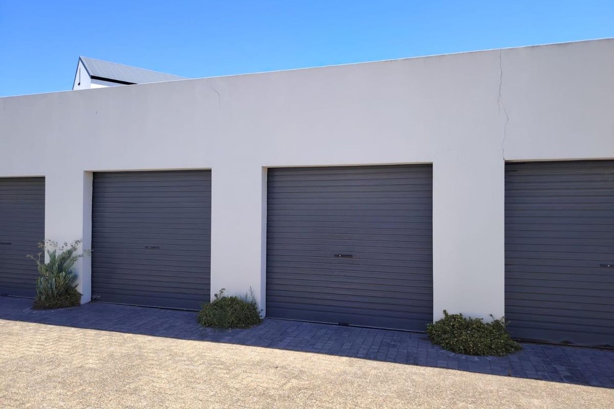 Exterior view of a multi-bay garage block featuring dark grey sectional doors and paved driveway access.