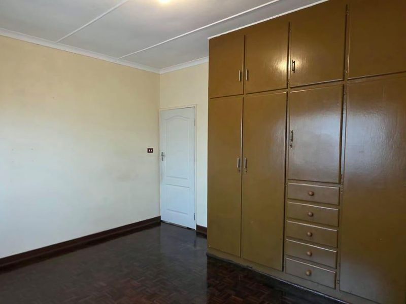 A vacant bedroom featuring original parquet flooring, coved ceilings, and extensive built-in wooden cabinetry providing ample storage space.