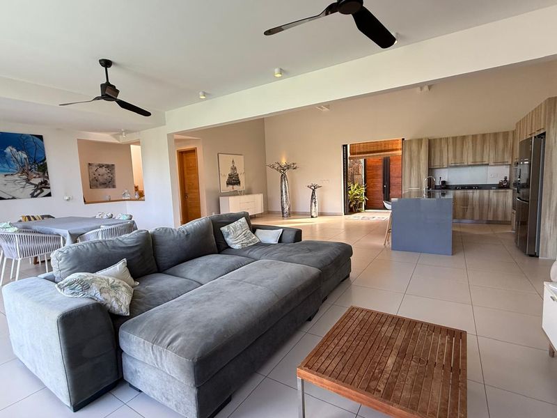Spacious open-plan living area featuring a modern kitchen with wood-finish cabinetry, a central island, and seamless flow to the outdoor space.