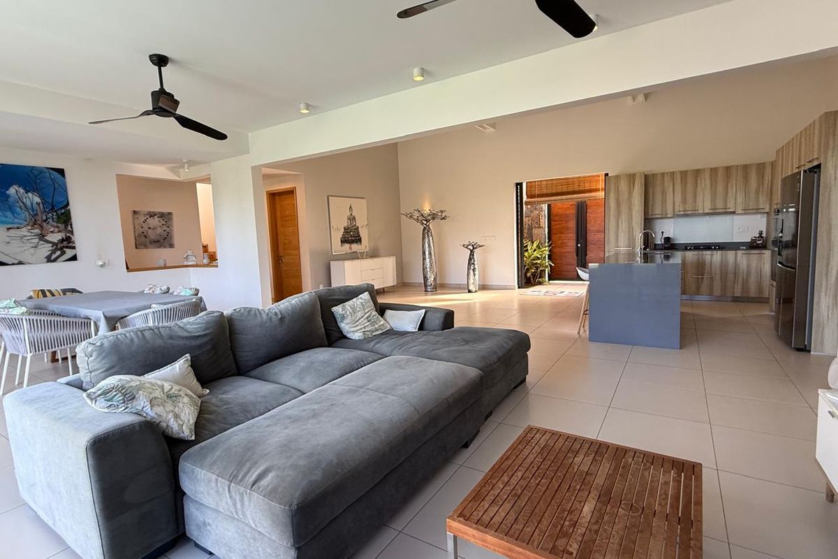 Spacious open-plan living area featuring a modern kitchen with wood-finish cabinetry, a central island, and seamless flow to the outdoor space.