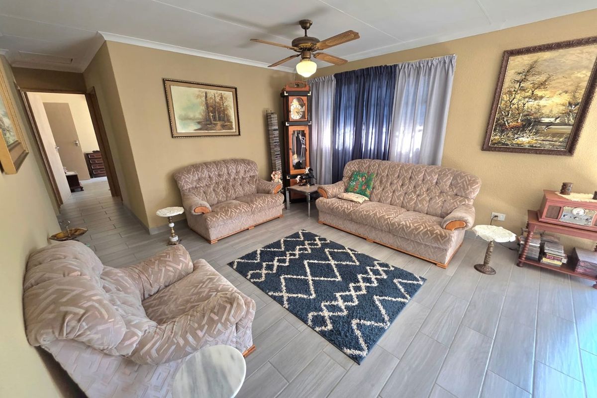 A spacious living room featuring neutral wall tones, modern grey tiled flooring, and a central ceiling fan, offering a comfortable and functional living space.