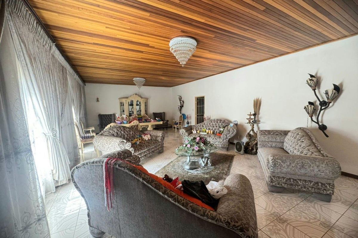 Spacious living room featuring a distinctive timber-paneled ceiling, decorative crystal chandeliers, and tiled flooring throughout.