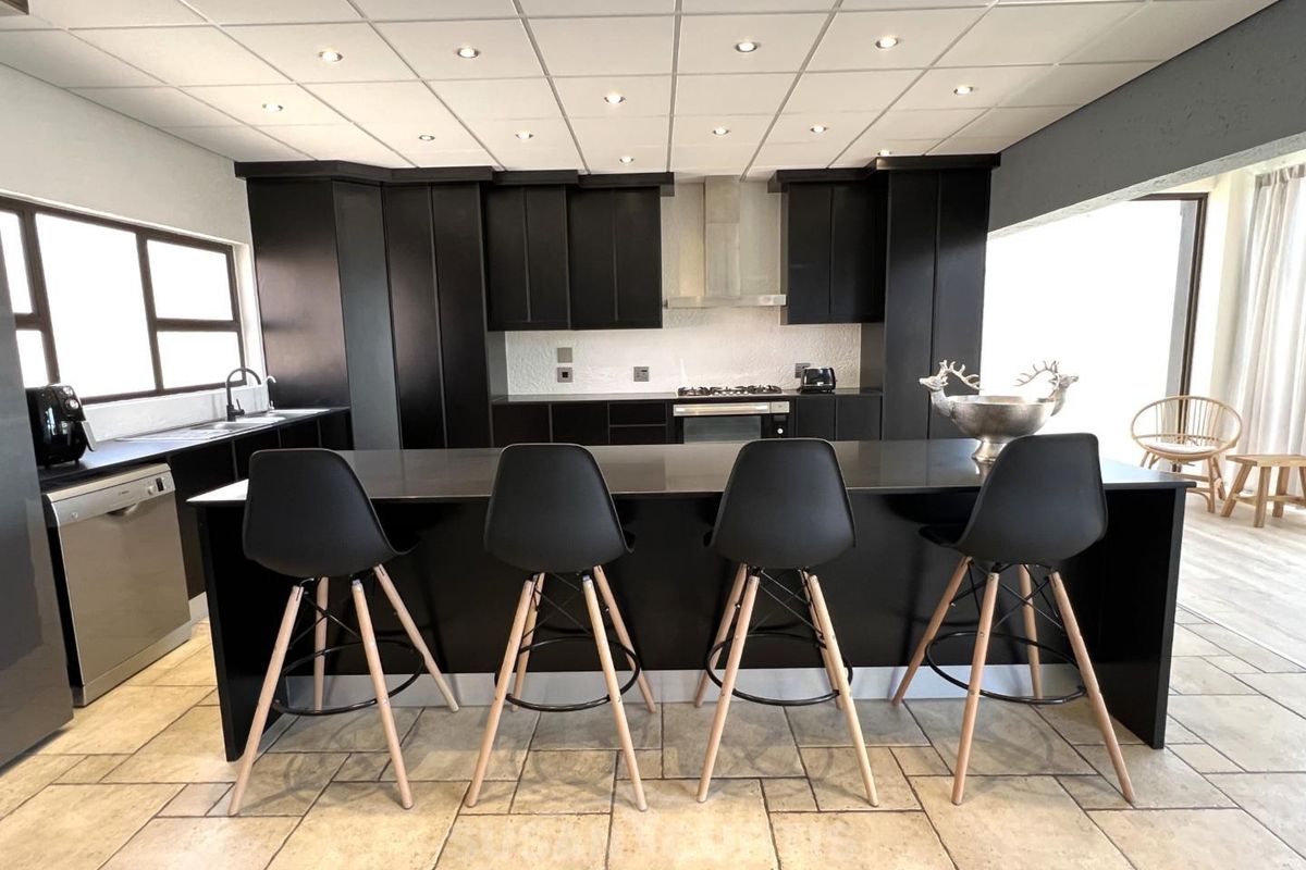Modern kitchen featuring dark cabinetry, a large central island with seating, integrated appliances, and tiled flooring under a drop ceiling with recessed lighting.