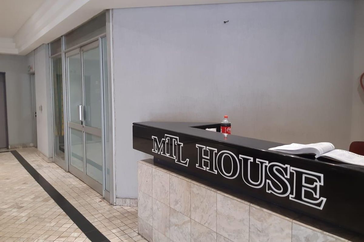 A professional building entrance featuring a tiled floor, glass-panelled doors, and a built-in reception desk with branded signage.