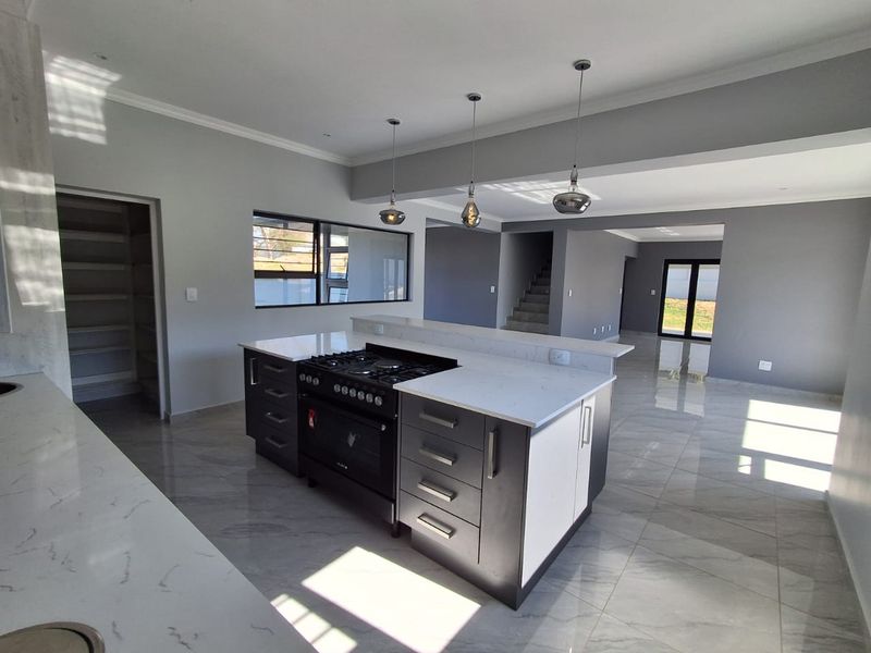 Modern open-plan kitchen featuring a central island with gas cooktop, stone countertops, and sleek cabinetry, flowing into a spacious living area with tiled floors.