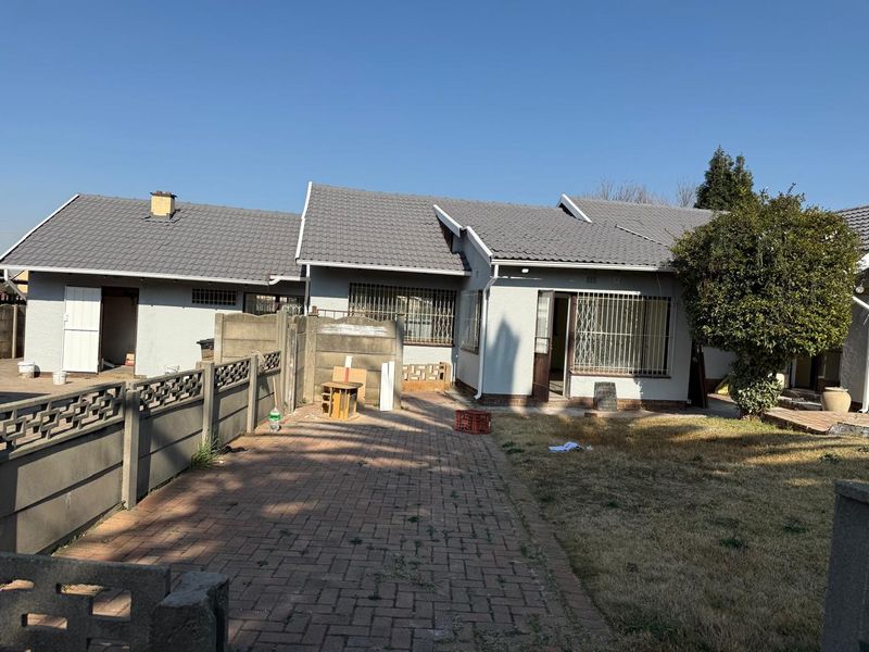 Rear view of the property featuring a tiled roof, paved patio area, and secure perimeter walling with security bars on windows.