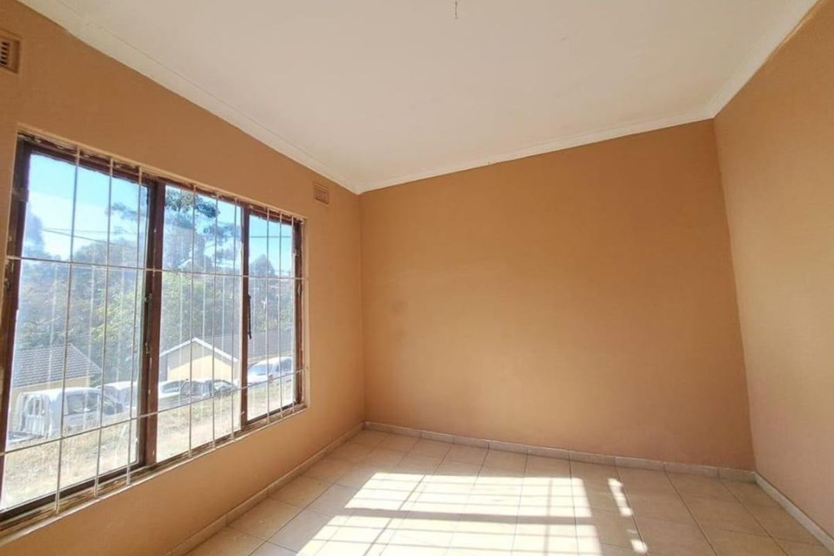 A vacant bedroom featuring tiled flooring, neutral wall paint, and large windows fitted with security bars, offering a blank canvas for personalization.