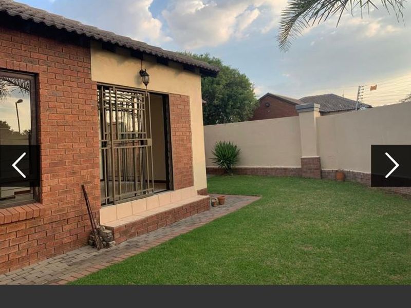A well-maintained rear exterior view featuring a face brick facade, paved walkway, and a private garden enclosed by a perimeter wall.