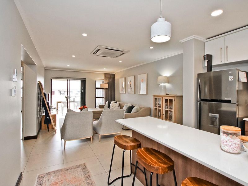 Modern open-plan living area featuring a sleek kitchen with stone island, recessed lighting, ducted air conditioning, and seamless flow to the outdoor patio.