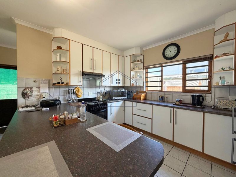 A functional kitchen featuring white cabinetry, laminate countertops, tiled backsplash, and a breakfast bar area with tiled flooring.