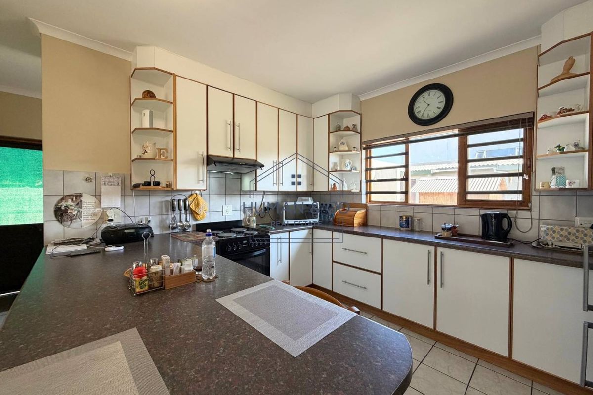 A functional kitchen featuring white cabinetry, laminate countertops, tiled backsplash, and a breakfast bar area with tiled flooring.