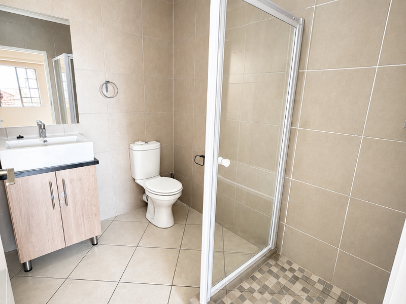 A clean, neutral-toned bathroom featuring a modern vanity, a toilet, and a glass-enclosed shower with mosaic floor tiling.