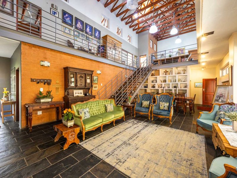 Spacious double-volume living area featuring exposed timber roof trusses, a mezzanine level, metal staircase, and distinctive slate tile flooring with an exposed brick feature wall.