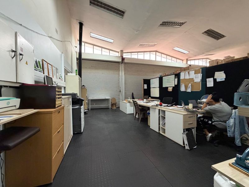 Open-plan office space featuring high ceilings with skylights, industrial roller shutter doors, and durable rubber flooring, suitable for a functional business environment.