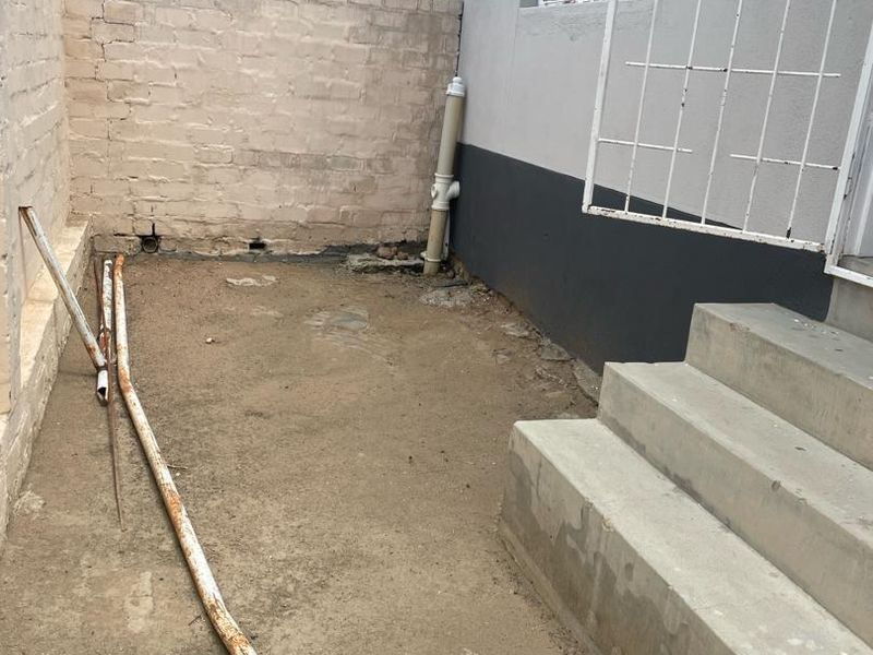 A rear exterior area featuring concrete steps, a security gate, and a brick boundary wall, currently requiring landscaping and surface finishing.