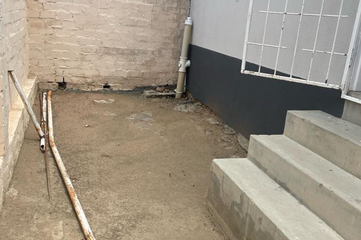 A rear exterior area featuring concrete steps, a security gate, and a brick boundary wall, currently requiring landscaping and surface finishing.