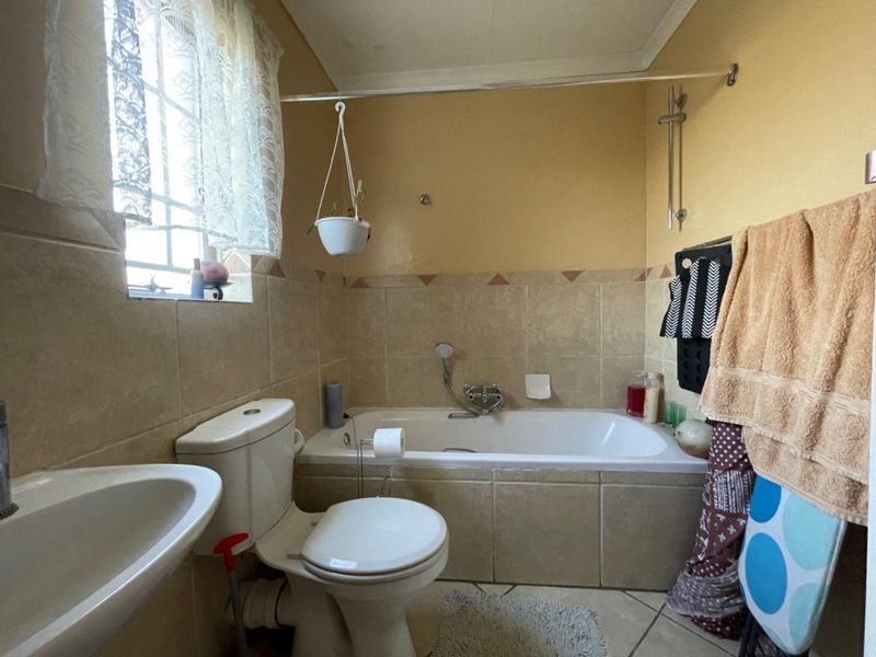 A functional bathroom featuring a bathtub with shower mixer, pedestal basin, and neutral wall and floor tiling.