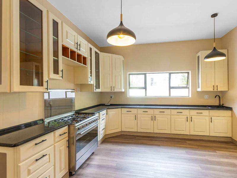 A clean, well-lit kitchen featuring cream-colored cabinetry, dark stone countertops, a gas stove, and modern pendant lighting over a spacious layout.