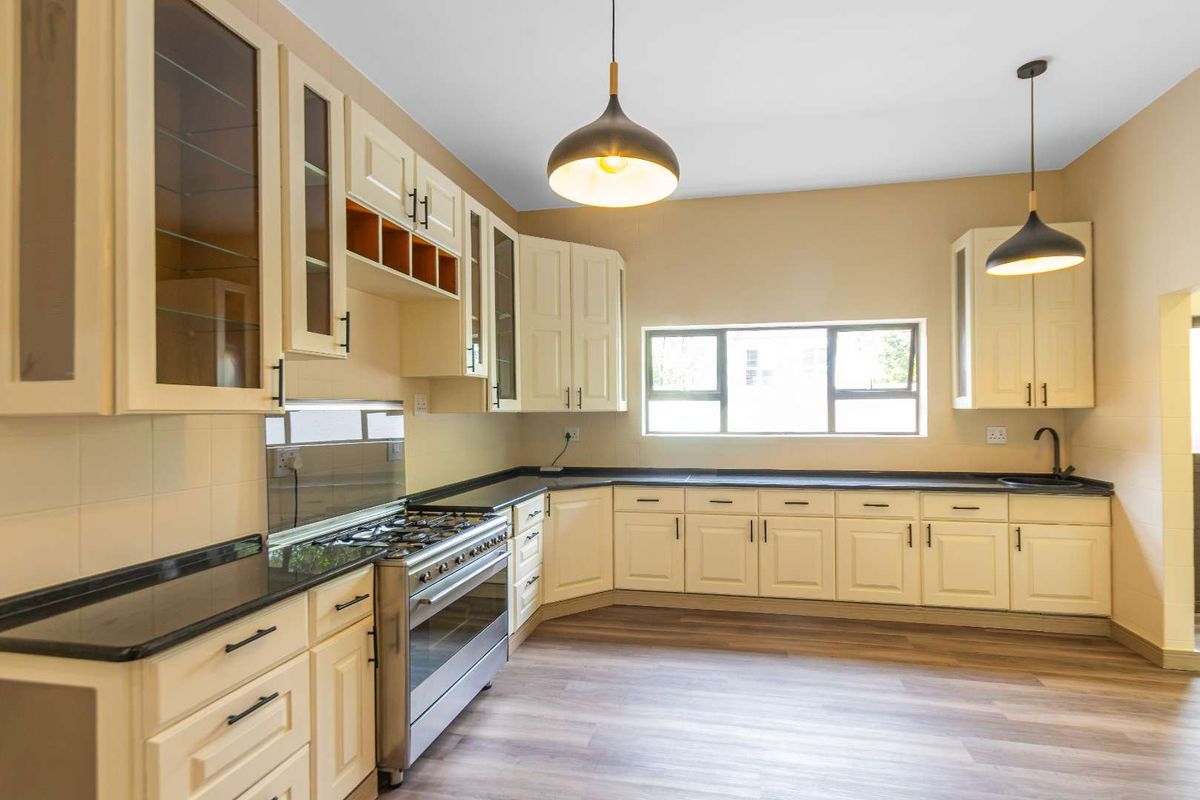A clean, well-lit kitchen featuring cream-colored cabinetry, dark stone countertops, a gas stove, and modern pendant lighting over a spacious layout.