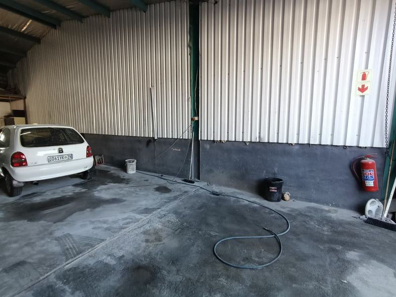 Spacious industrial garage area featuring corrugated metal wall cladding, concrete flooring, and an exposed steel roof structure, suitable for storage or workshop use.