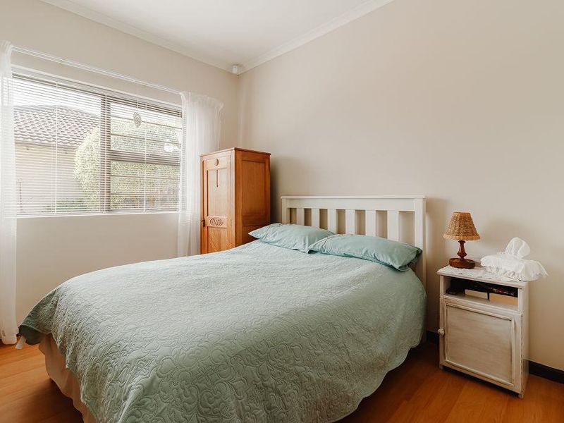 A well-lit bedroom featuring laminate flooring, neutral walls, and an aluminium-framed window with venetian blinds.