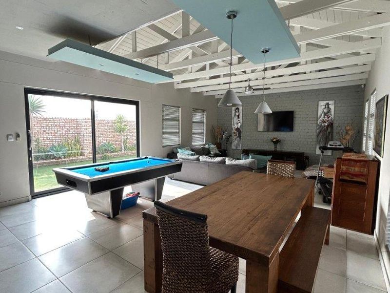 Spacious open-plan living and dining area featuring exposed timber rafters, tiled flooring, a brick feature wall, and large sliding doors leading to the garden.