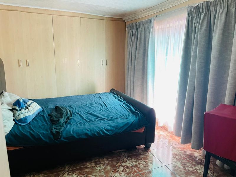 A bedroom featuring built-in cupboards, tiled flooring, and decorative ceiling cornice, providing a functional space with natural light from the window.