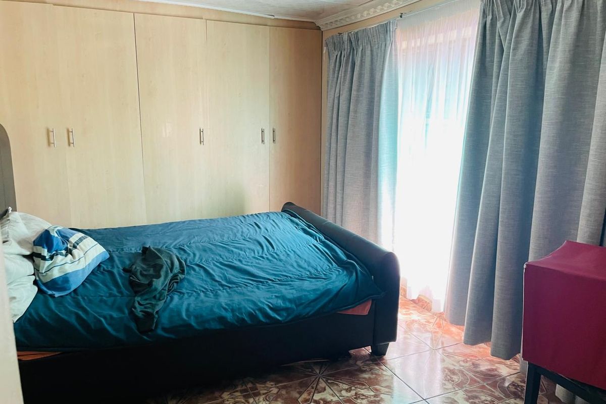 A bedroom featuring built-in cupboards, tiled flooring, and decorative ceiling cornice, providing a functional space with natural light from the window.