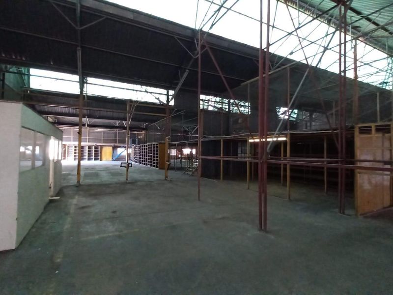 Expansive industrial warehouse space featuring high ceilings with exposed steel trusses, concrete flooring, and integrated shelving units suitable for storage or manufacturing operations.