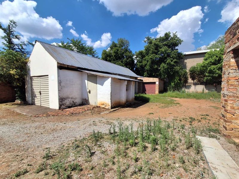 Rear exterior view of a detached outbuilding or garage with a corrugated metal roof, showing signs of significant wear and maintenance requirements.