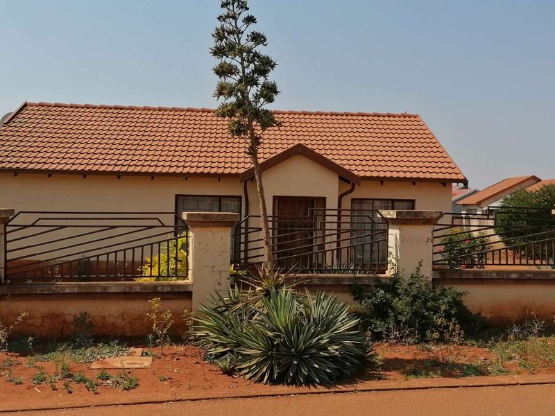 Front elevation of a single-story house featuring a tiled roof, perimeter wall with metal fencing, and a gated entrance.