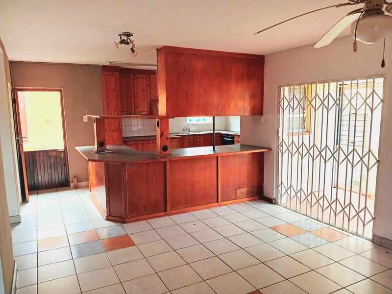 Open plan kitchen and living area featuring wooden cabinetry, a breakfast bar, tiled flooring, and a security gate leading to the exterior.