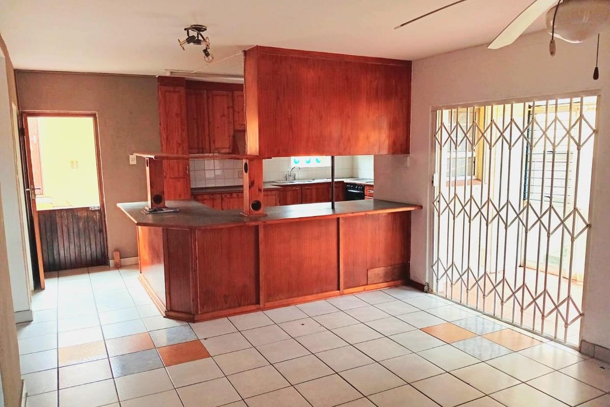 Open plan kitchen and living area featuring wooden cabinetry, a breakfast bar, tiled flooring, and a security gate leading to the exterior.