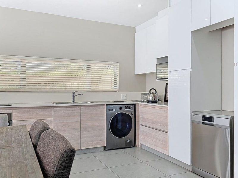 Modern kitchen featuring sleek white cabinetry, light wood-grain base units, tiled flooring, and integrated appliances including a dishwasher and washing machine.