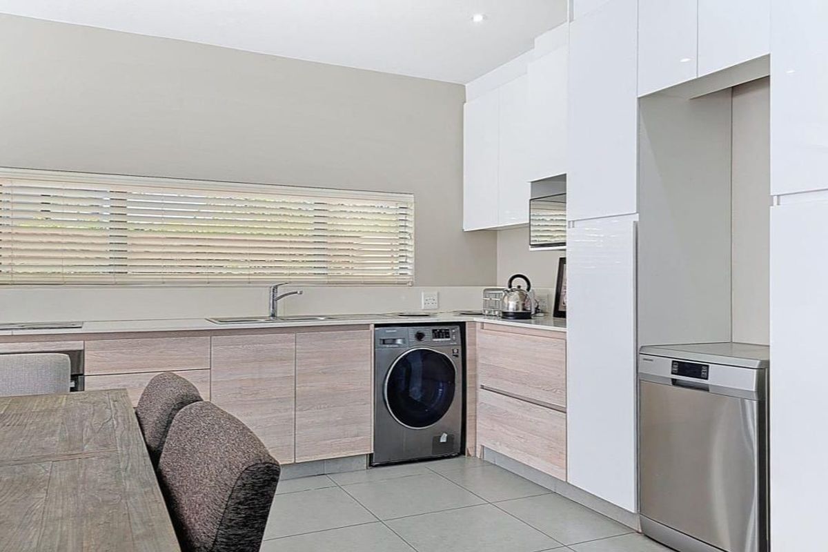 Modern kitchen featuring sleek white cabinetry, light wood-grain base units, tiled flooring, and integrated appliances including a dishwasher and washing machine.