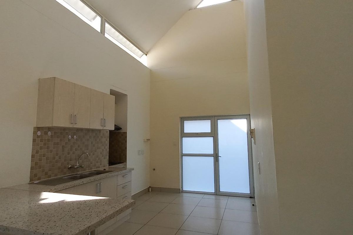 An open-plan kitchen and living area featuring vaulted ceilings, clerestory windows for natural light, tiled flooring, and a functional kitchen layout with neutral cabinetry.