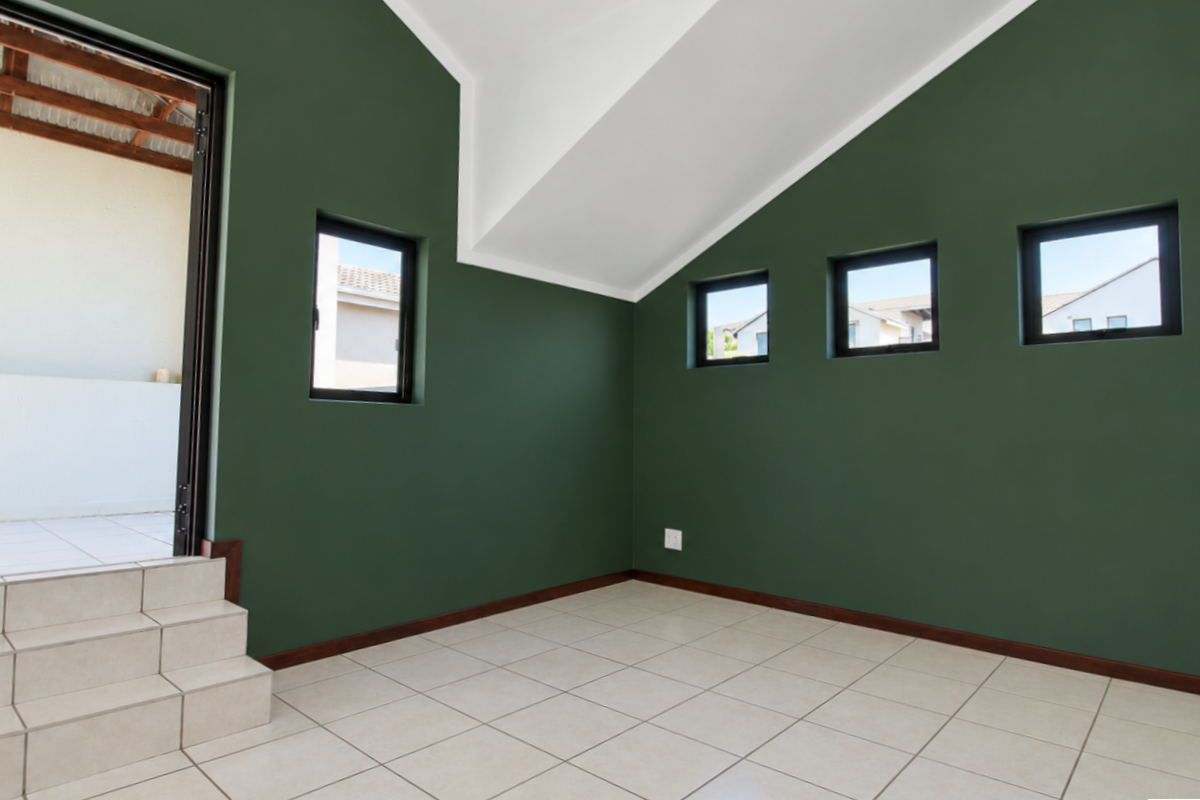 An empty living area featuring vaulted ceilings, tiled flooring, and large windows, with a stepped entrance leading to an outdoor space.