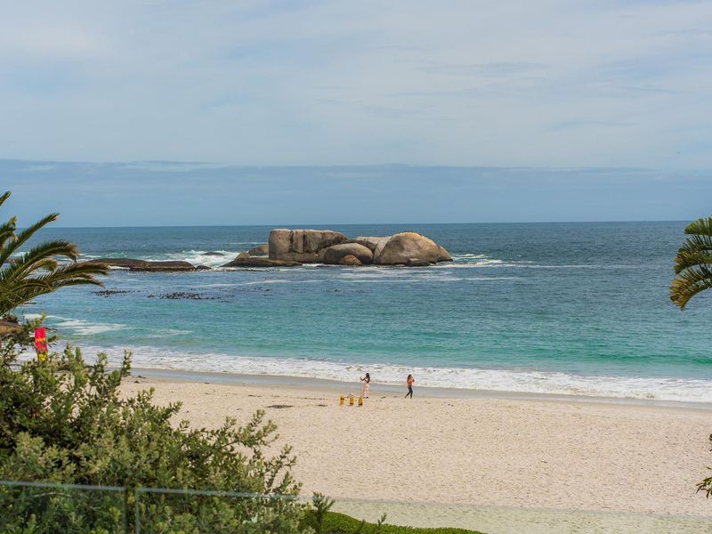 A scenic view of the ocean, sandy beach, and rock formations, framed by coastal vegetation.