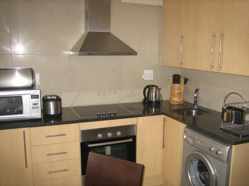 Compact kitchen featuring light wood cabinetry, granite countertops, stainless steel appliances, and a tiled backsplash.